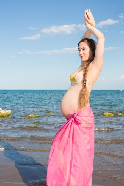 Donna incinta con capelli lunghi che medita in una posa di yoga sul mare