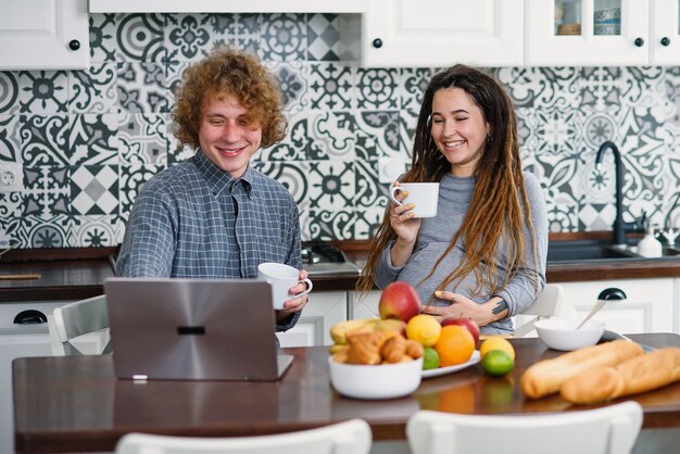 Donna incinta con i dreadlocks e il marito riccio in una cucina moderna che cucina dietro fresco e