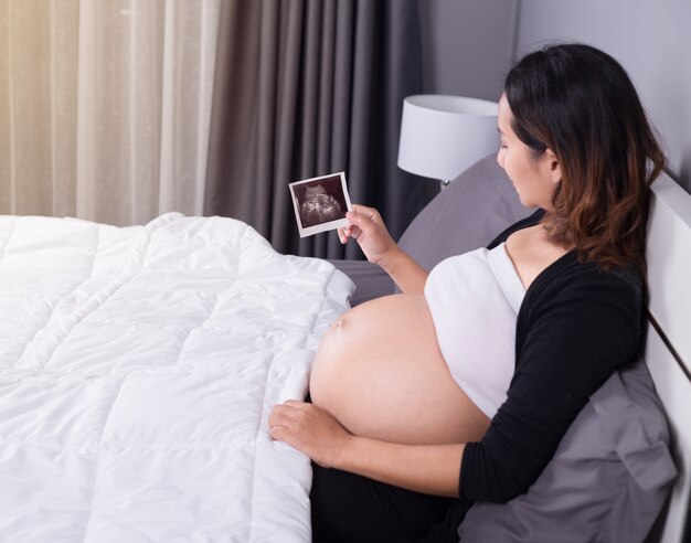 donna incinta con l&#39;immagine di ultrasuono di fare da baby-sitter sul letto in camera da letto a casa