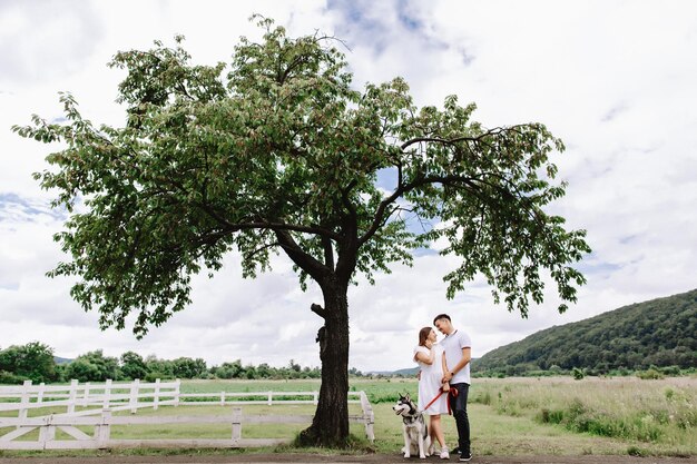 Donna incinta con marito e cane husky vicino all'albero in natura