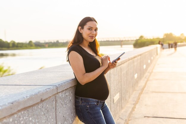 Donna incinta con smartphone all'aperto tecnologia di gravidanza e concetto di comunicazione