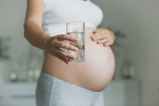 Donna incinta del primo piano che tiene bicchiere d'acqua