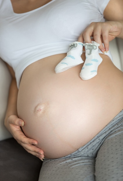 Donna incinta del primo piano che tiene i calzini del bambino sulla pancia