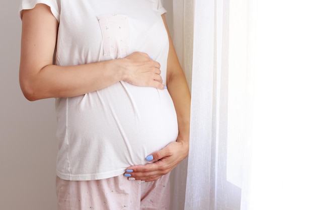 Donna incinta del primo piano che tiene la sua pancia alla finestra