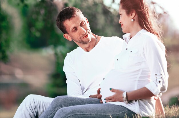 Donna incinta e felice futuro padre seduto sull'erba nel parco in una giornata di sole