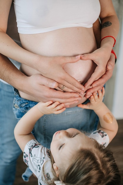 Donna incinta e figlia piccola che tengono un cuore con le mani sullo stomacoxA