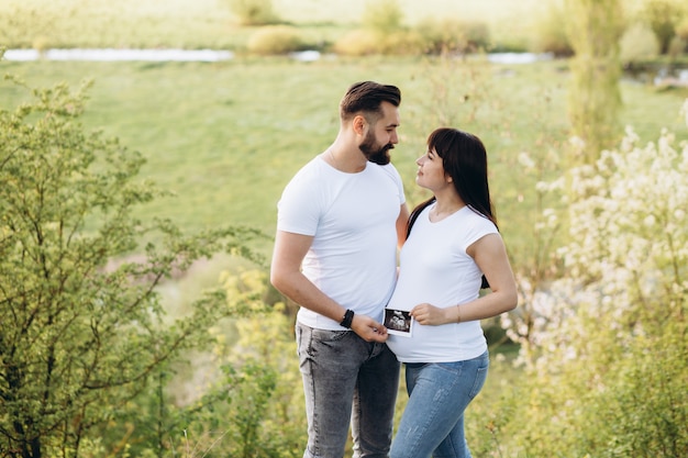 Donna incinta e il suo beaeded marito abbracciarsi sulla pancia insieme nella natura all&#39;aperto