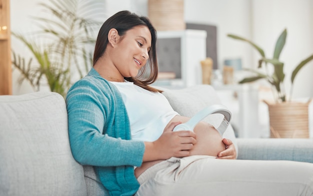 Donna incinta e pancia con le cuffie per la musica per il suo bambino non ancora nato mentre si rilassa a casa Pancione e gravidanza con una madre che utilizza un auricolare per lo streaming audio o podcast
