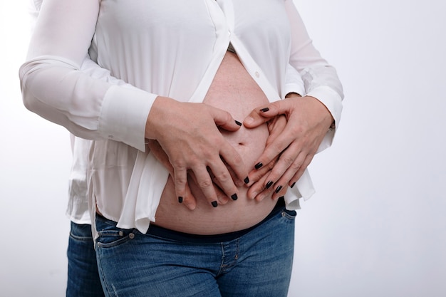 Donna incinta e suo marito che si tengono per mano sulla pancia. Coppia in attesa di un bambino in studio con sfondo bianco