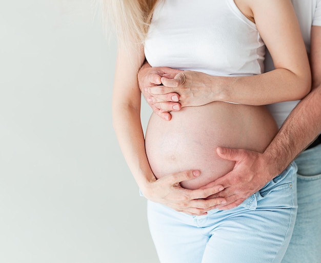 Donna incinta e suo marito che tengono insieme la mano 2 mani che tengono il bambino all'interno di una donna incinta amore per la famiglia Parenting