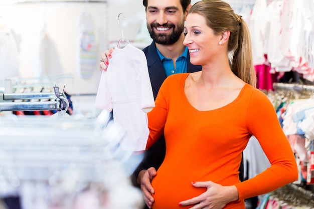 Donna incinta e uomo che compra vestiti del bambino in negozio