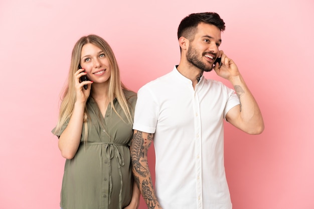 Donna incinta e uomo su sfondo rosa isolato parlando al cellulare