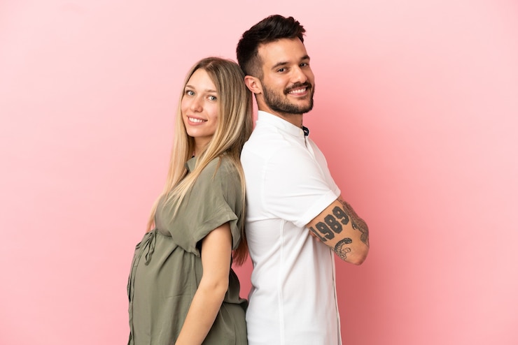Foto donna incinta e uomo su sfondo rosa isolato tenendo le braccia incrociate