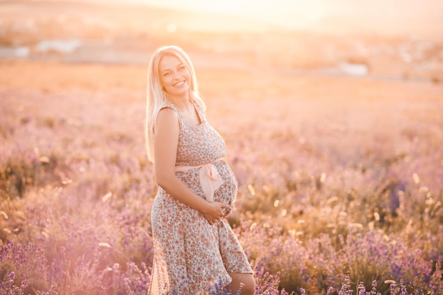 Donna incinta felice che posa nel campo di lavanda all'aperto