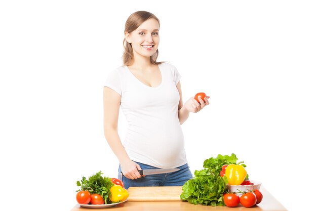 Donna incinta felice che prepara insalata. Colpo dello studio, isolato