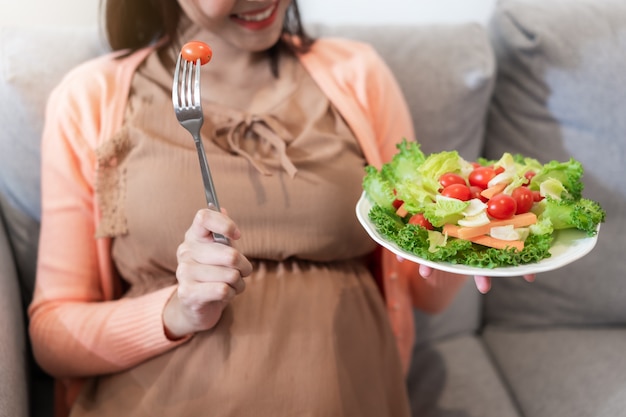 Donna incinta felice che si siede e che mangia insalata di verdure naturale