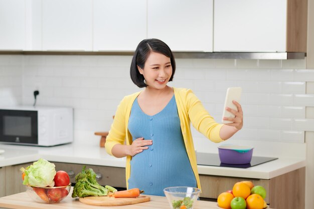 Donna incinta in cucina che prepara il cibo utilizzando il telefono cellulare