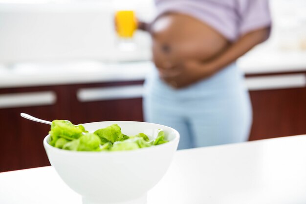 Donna incinta in cucina con insalata sul tavolo a casa