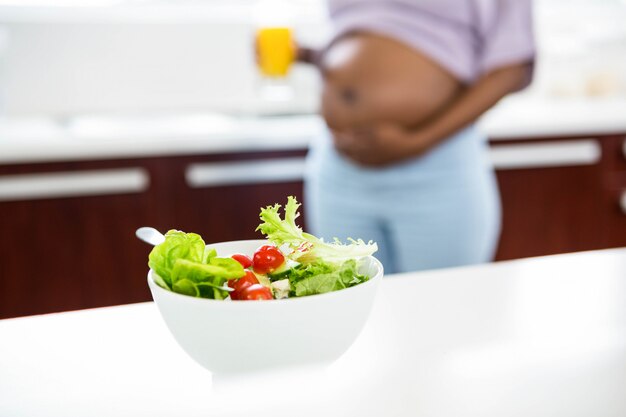 Donna incinta in cucina con insalata sul tavolo a casa