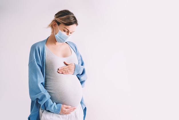 donna incinta in maschera medica che abbraccia pancia gravidanza e parto durante malattie infettive