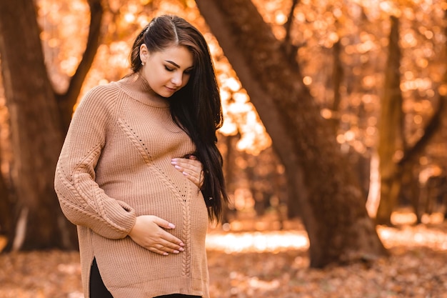 Donna incinta in piedi nella foresta del parco cittadino di autunno, tenendo accarezzando la sua pancia rotonda con il bambino