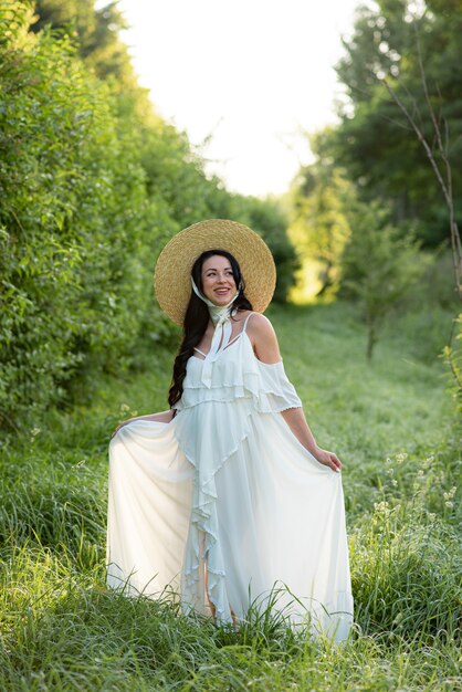 Donna incinta in posa in un abito bianco su uno sfondo di natura.