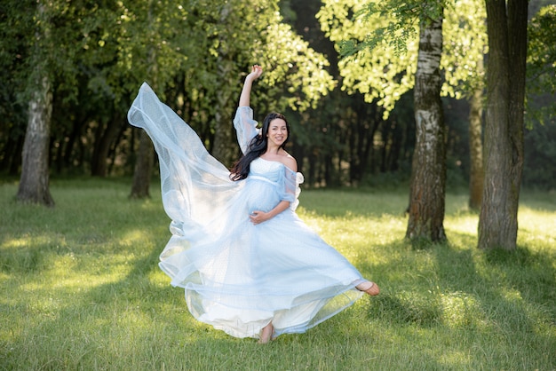 Donna incinta in posa in un abito blu con alberi verdi.