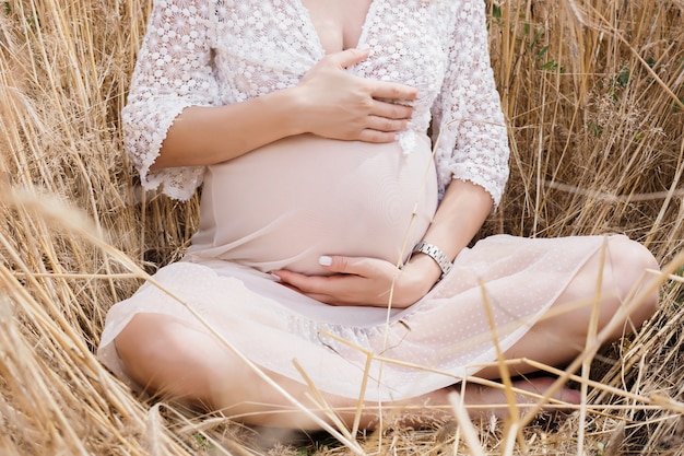 Donna incinta in un campo di grano. Mani della madre sul ventre. Concetto di bambino in attesa.