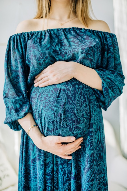 Donna incinta in vestito blu che tiene il suo stomaco.