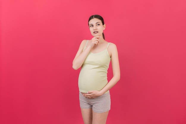 Donna incinta pensierosa che sceglie il nome per il bambino su sfondo colorato Sogno e donna incinta felice che pensa immaginando lo spazio della copia della vita della maternità