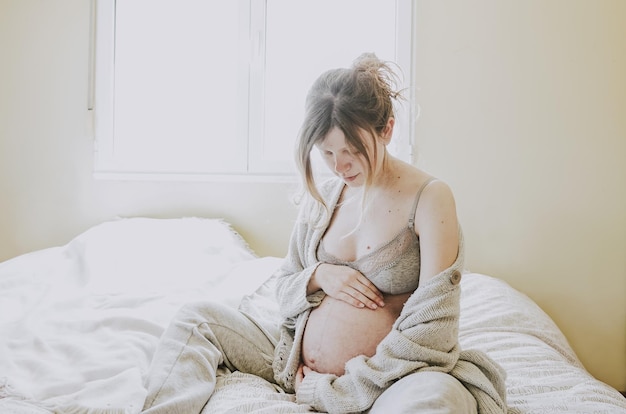 Donna incinta seduta a letto a casa