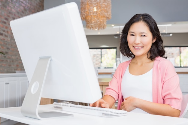 Donna incinta sorridente che per mezzo del computer a casa