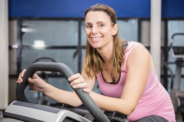 Donna incinta sorridente che si siede sulla cyclette in palestra