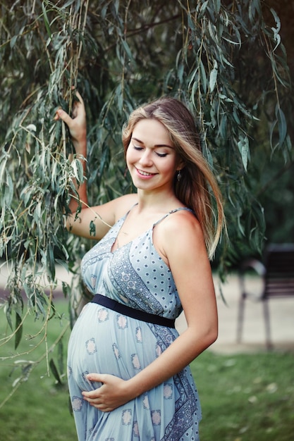 Donna incinta sorridente che tocca l'addome mentre è in piedi sull'erba