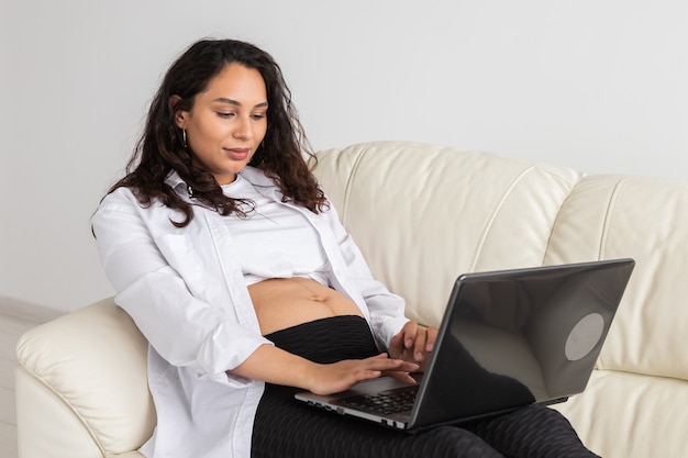 Donna incinta utilizzando laptop mentre è seduto su un divano nel soggiorno di casa.