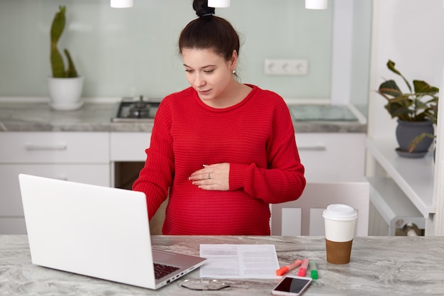 Donna incinta vestita in maglione rosso, lavora da casa