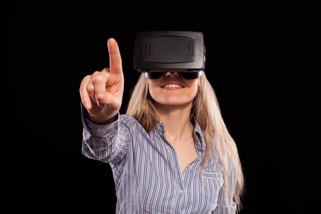 Donna incuriosita che indossa cuffie 3D per realtà virtuale ed esplora il gioco su sfondo nero