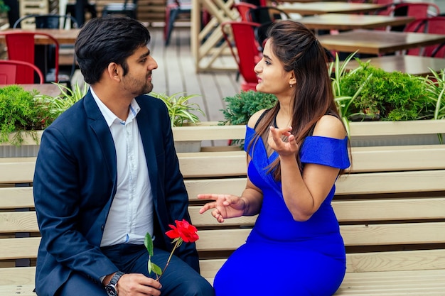 Donna indiana bruna dai capelli lunghi in abito blu con il suo bel ragazzo che frequenta appuntamenti annoiandosi .uomo che dà rose alla sua ragazza cattiva relazione in una strada estiva del centro.