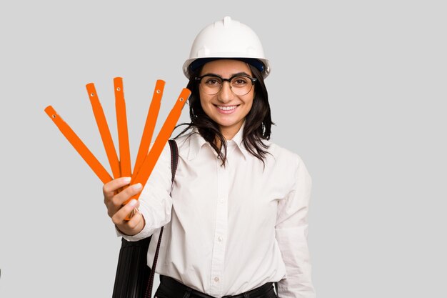 Donna indiana del giovane architetto con il casco e che tiene un metro tagliato isolato