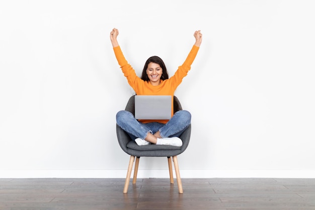 Donna indiana emotiva che utilizza il computer portatile alzando le mani