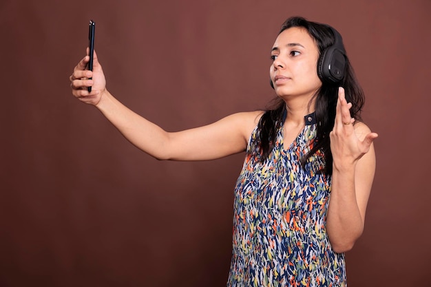 Donna indiana in cuffia che chatta sulla videoconferenza dello smartphone, gesticolando, parlando in videochiamata. Persona che indossa auricolari wireless, telefono cellulare in mano, comunicazione remota