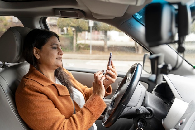 Donna indiana matura occupata che tiene il telefono cellulare alla guida dell'auto Trasporto distratto alla guida