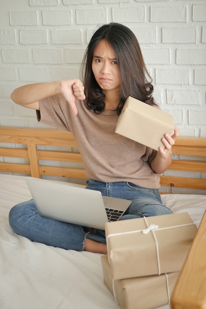 Donna infelice che dà il pollice giù gesto con il computer e la cassetta dei pacchi del prodotto a casa