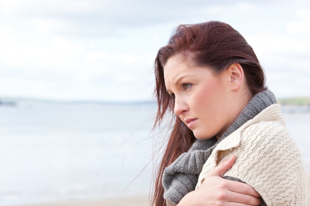 Donna infelice che indossa cappello e sciarpa sulla spiaggia