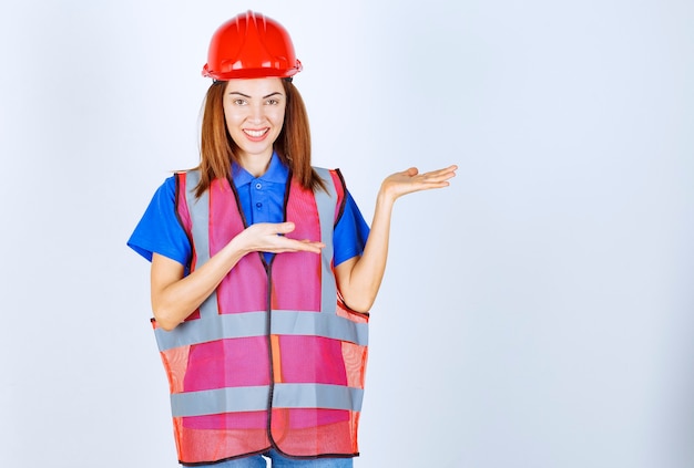 Donna ingegnere in uniforme e casco rosso che punta a qualcuno sulla destra.