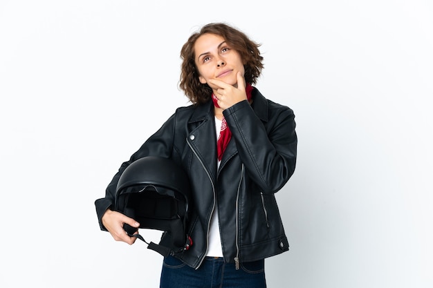 Donna inglese che tiene un casco del motociclo isolato su priorità bassa bianca che ha dubbi