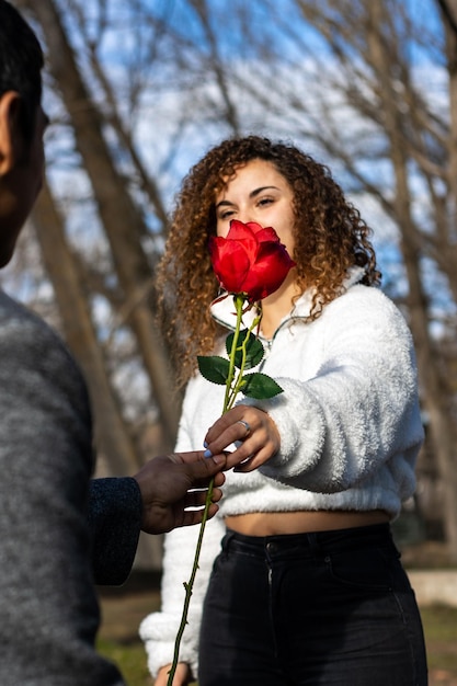 Donna innamorata che dà una rosa al suo ragazzo Sorridente ragazza innamorata che dà una rosa al suo ragazzo all'aperto