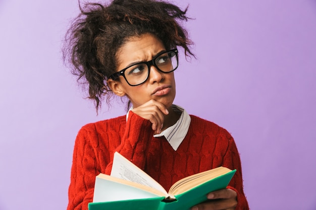 Donna intelligente afroamericana in uniforme scolastica che tiene e libro di lettura, isolato