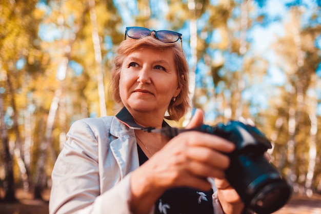 Donna invecchiata mezzo che controlla le immagini sulla macchina fotografica nella foresta di autunno