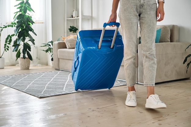 Donna irriconoscibile che esce di casa con una valigia che va in viaggio o in vacanza